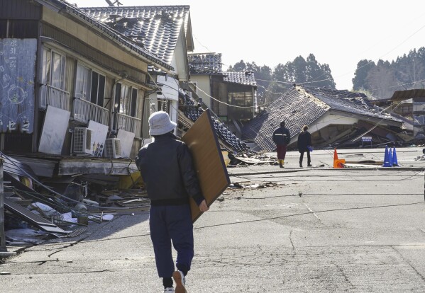 A resident carries belongings in Suzu, Ishikawa prefecture, Japan Friday, Jan. 5, 2024. Monday’s temblor decimated houses, twisted and scarred roads and scattered boats like toys in the waters, and prompted tsunami warnings. (Kyodo News via AP)