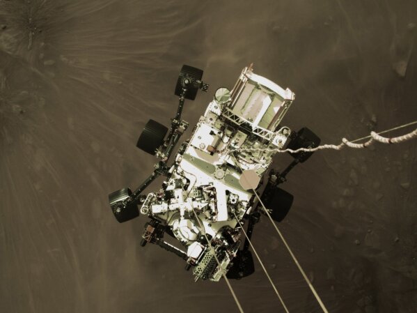 This Thursday, Feb. 18, 2021 photo provided by NASA shows the Perseverance rover lowered towards the surface of Mars during its powered descent. (NASA via AP)