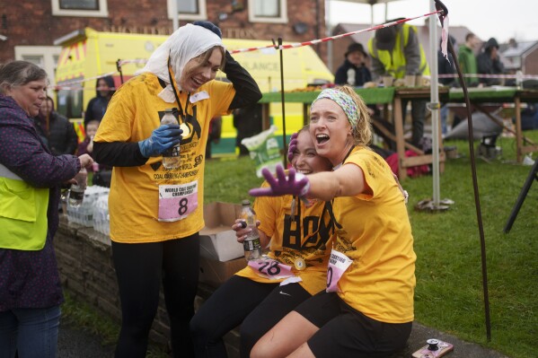 Women's race contestants react at the finish after running with 20kg sacks of coal over a 1.1 km course during the World Coal Carrying Championships in Ossett, West Yorkshire, England, Monday, April 21, 2025. (AP Photo/Jon Super)