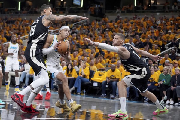 Indiana Pacers' Andrew Nembhard, center, heads to the basket past Milwaukee Bucks' Kyle Kuzma (18) and Brook Lopez, right, during the first half of a first-round NBA basketball playoff game, Saturday, April 19, 2025, in Indianapolis. (AP Photo/Michael Conroy)