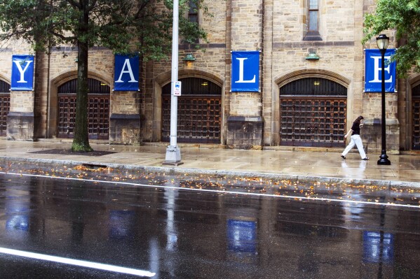 FILE - A woman walks by a Yale sign reflected in the rainwater on the Yale University campus, Aug. 22, 2021, in New Haven, Conn. Connecticut lawmakers are considering banning the use of legacy and donor preferences in admissions to all colleges and universities across the state, including private ones like Yale University. (AP Photo/Ted Shaffrey, File)