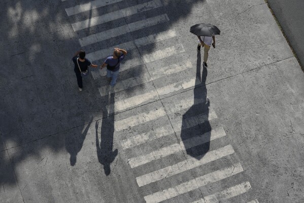A man uses an umbrella to shield him from the afternoon sun in Manila, Philippines on Thursday, July 6, 2023. (AP Photo/Aaron Favila)
