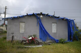 FILE - In this May 28, 2020 file photo, the home of 85-year-old Carmen Lacen, sits inhabitable after the passing of Hurricane Maria partially covered by a torn, blue tarp, in Loiza, Puerto Rico. The U.S. territory is slated to receive more than $6 billion in federal funds to help prepare for future hurricanes and other disasters, officials said Tuesday, Feb. 2, 2021. (AP Photo/Carlos Giusti, File)