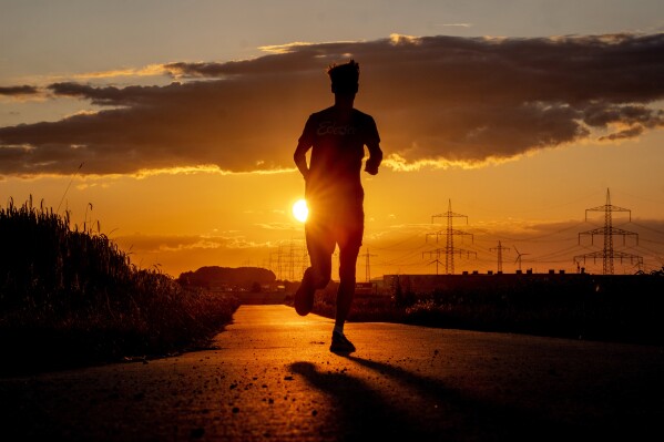 A man runs along a small road on the outskirts of Frankfurt, Germany, as the sun rises early Thursday, July 13, 2023. (AP Photo/Michael Probst)