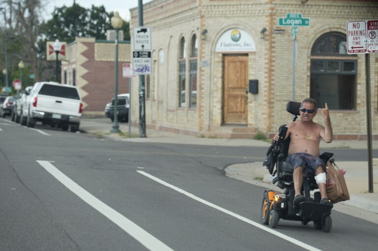 Un hombre sin camisa guía su silla de ruedas por el carril para bicicletas a lo largo de la Avenida 45 mientras las temperaturas suben a tres dígitos en el vecindario de Globeville el miércoles 26 de julio de 2023, en el norte de Denver.  (Foto AP/David Zalubowski)