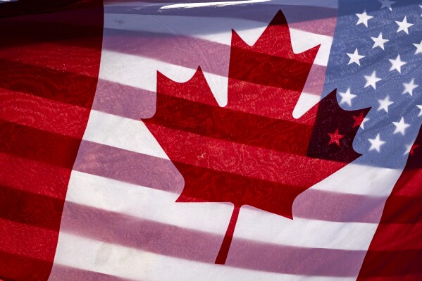 Sunlight shines through the flags of Canada and the United States, held together by a protester outside on Parliament Hill in Ottawa, Feb. 1, 2025.(Justin Tang/The Canadian Press via AP, File)