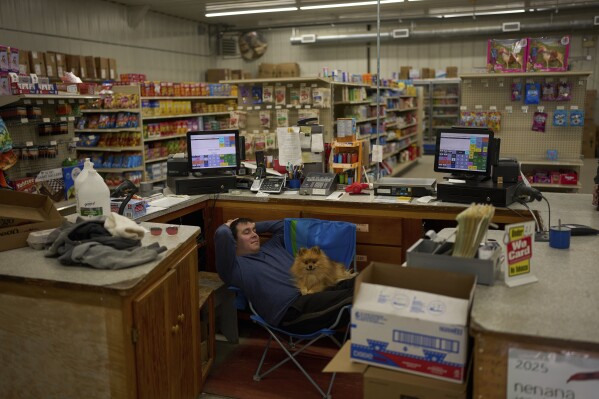 Brenden Sweetsir waits with dog Rex for customers at Sweetsirs store Wednesday, May 21, 2025, in Galena, Alaska. (AP Photo/John Locher)