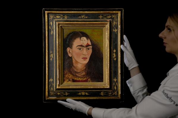 FILE - A staff member poses for photographs with the Mexican painter Frida Kahlo's 1949 self-portrait "Diego y yo", Diego and I, at Sotheby's auction house in London, Thursday, Oct. 21, 2021.  The Mexican icon, whose art is as immediate and unsentimental as her own fight with adversity, will be the subject of an upcoming musical with music by Mexican composer Jaime Lozano and lyrics by the Obie Award-winning playwright Neena Beber, The Associated Press has learned, Thursday, July 21, 2022.  (AP Photo/Matt Dunham, File)