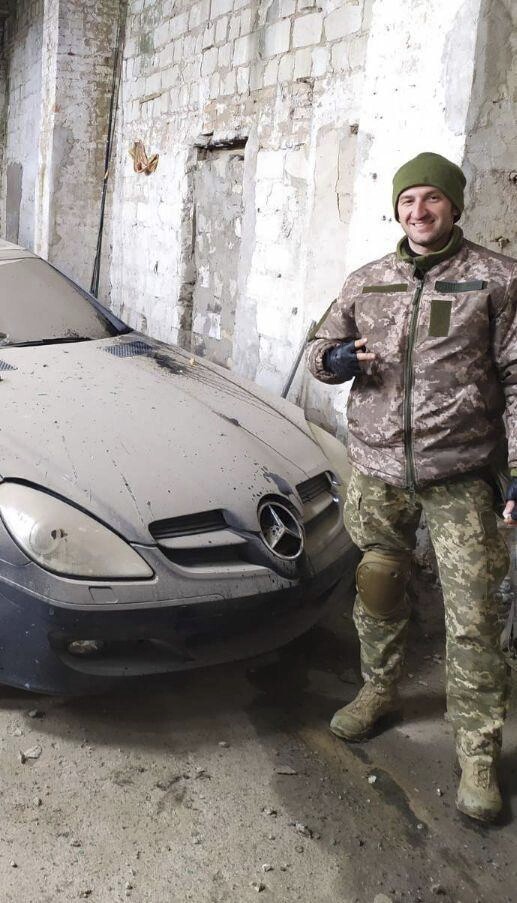 ADDS DATE AND LOCATION In this photo from April 2022 provided by his family, Oleksandr “Sasha” Romanovych Hrysiuk, in uniform, poses next to a luxury automobile in Ukraine's Mykolaiv region. Soldiers from Sasha's unit said they were very sorry they couldn't take his body with them, the shelling was too heavy, all they could do was hide him in a cellar in Dovhenke – a rural settlement in eastern Ukraine that fell to the Russians. (Courtesy Olha Hrysiuk via AP)