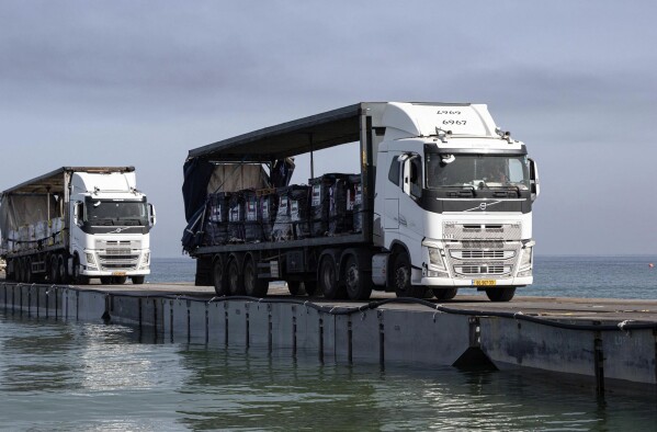 FILE - This image provided by the U.S. Army shows trucks loaded with humanitarian aid from the United Arab Emirates and the United States Agency for International Development cross the Trident Pier before arriving on the beach on the Gaza Strip, May 17, 2024. A key section of the U.S. military-built pier designed to carry badly needed aid into Gaza by boat has been reconnected to the Gaza beach following storm damage repairs and aid will begin to flow soon, the U.S. Central Command announced Friday. (Staff Sgt. Malcolm Cohens-Ashley/U.S. Army via AP, File)