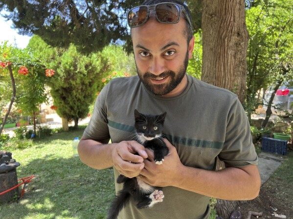 In this photo provided by Reuters, Issam Abdallah, a videographer for the news agency, holds a kitten while posing for a picture in Saaideh, Lebanon, on July 4, 2023. Abdallah was killed Friday, Oct. 13, 2023, when an Israeli shell landed in a gathering of international journalists covering clashes on the border in south Lebanon. Six other journalists were injured in the incident. (Emilie Madi/Reuters via AP)