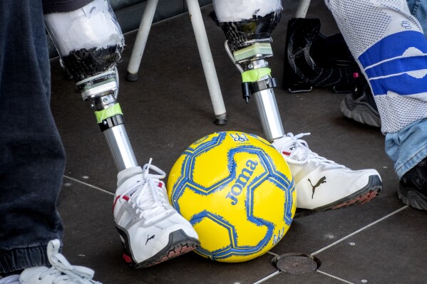 A Ukrainian war veteran with prosthetic legs watch players of Ukraine's national soccer team during a public training session in Wiesbaden, Germany, Thursday, June 13, 2024, ahead of their group E match against Romania at the Euro 2024 soccer tournament. (AP Photo/Michael Probst)