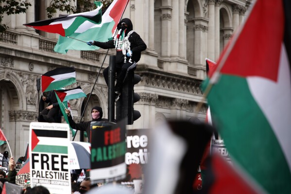 Demonstrators hold up flags and placards as they stand on traffic lights near Downing Street during a pro Palestinian demonstration in London, Saturday, Oct. 21, 2023. (AP Photo/David Cliff)