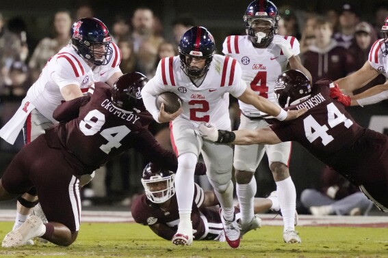 Mississippi quarterback Jaxson Dart (2) dodges Mississippi State defensive tackle Jaden Crumedy (94) and linebacker Jett Johnson (44) on a short gain during the first half of an NCAA college game in Starkville, Miss., Thursday, Nov. 23, 2023. (AP Photo/Rogelio V. Solis)