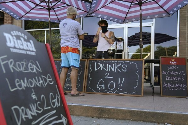 A drinks-to-go table is set up outside the Old Crow bar on Greenville Avenue in Dallas, Thursday, Aug. 13, 2020. Some states and cities in the U.S. are allowing cocktails to-go due to the pandemic. (AP Photo/LM Otero)