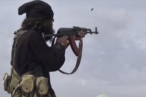 FILE - This file frame grab from video posted online March 18, 2019, by the Aamaq News Agency, a media arm of the Islamic State group, shows an IS fighter firing his weapon during clashes with the U.S.-backed Syrian Democratic Forces (SDF) fighters, in Baghouz, Syria. Gunmen ambushed a bus carrying Syrian soldiers early Friday, Aug. 11, 2023 in the country’s east, killing at least 20 and wounding others, opposition activists said. The attack was believed to be carried out by members of the Islamic State group whose sleeper cells in parts of Syria still carry deadly attacks despite their defeat in 2019. (Aamaq News Agency via AP, File)