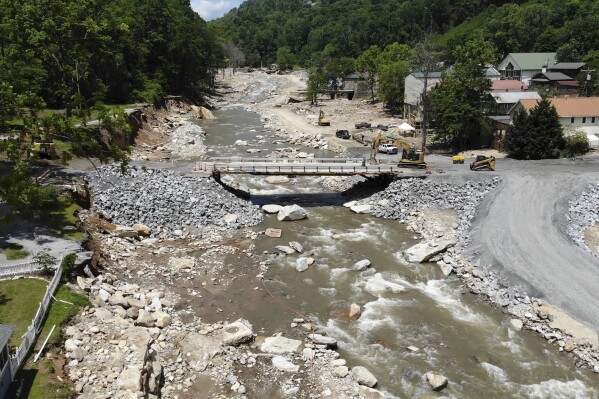 The Broad River flows beneath a temporary bridge beside flood-damaged buildings in Chimney Rock Village, N.C., on Wednesday, May 14, 2025. (AP Photo/Allen G. Breed)