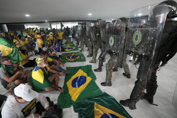 FILE - Supporters of Brazil's former President Jair Bolsonaro sit in front of a line of military police inside Planalto Palace after storming the official workplace of the president in Brasilia, Brazil, Sunday, Jan. 8, 2023. Brazil's federal police on Aug. 18, 2923 arrested seven senior military police officers accused of assisting right-wing rioters during the Jan. 8 attacks on government buildings. (AP Photo/Eraldo Peres, File)