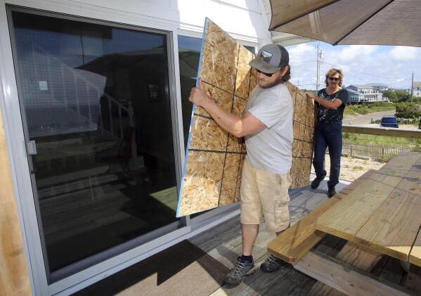 James Masog, center, and Gary Tavares, right, move particle board into place to board up the sliding glass doors of a clients house in Charlestown, R.I., ahead of Hurricane Henri, Saturday, Aug. 21, 2021. New Englanders, bracing for their first direct hit by a hurricane in 30 years, are taking precautions as Tropical Storm Henri barrels toward the southern New England coast. (AP Photo/Stew Milne)
