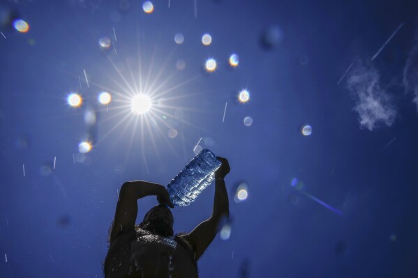 FILE - A man pours cold water onto his head to cool off on a sweltering hot day in the Mediterranean Sea in Beirut, Lebanon, July 16, 2023. As temperatures and humidity soar outside, what's happening inside the human body can become a life-or-death battle decided by just a few degrees. (ĢӰԺ Photo/Hassan Ammar, File)