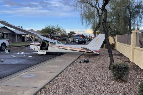 This photo provided by Goodyear Police Department shows a plane after an emergency crash landing on a neighborhood street in Goodyear, Ariz., Saturday, Feb. 10, 2024. The single engine plane experienced mechanical problems shortly after takeoff from nearby Glendale Airport, police said. The pilot and lone passenger escaped injury. (Goodyear Police Department via AP)