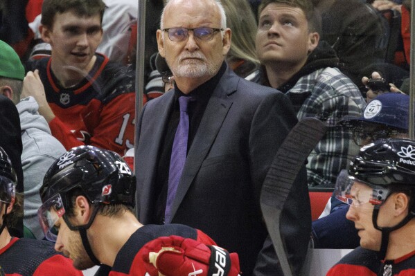 FILE - New Jersey Devils head coach Lindy Ruff, center, looks toward the ice during the third period of an NHL hockey game against the Carolina Hurricanes in Raleigh, N.C., Feb. 10, 2024. Ruff is returning to Buffalo for a second stint as coach of the Sabres. General manager Kevyn Adams announced the hiring Monday, April 22, 2024. (AP Photo/Ben McKeown, File)