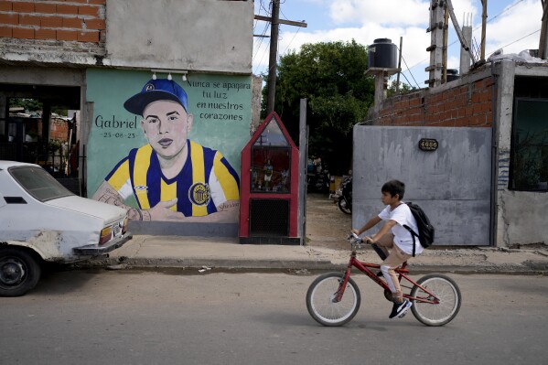 A child rides a bicycle past a mural of Gabriel Ignacio Romero, a resident who was murdered on the sidewalk outside his home the previous year, in Rosario, Argentina, Monday, April 8, 2024. For the past decade, the 1.3 million residents of Rosario have watched warily as presidents and their promises come and go. What endures, they say, is violence. (AP Photo/Natacha Pisarenko)