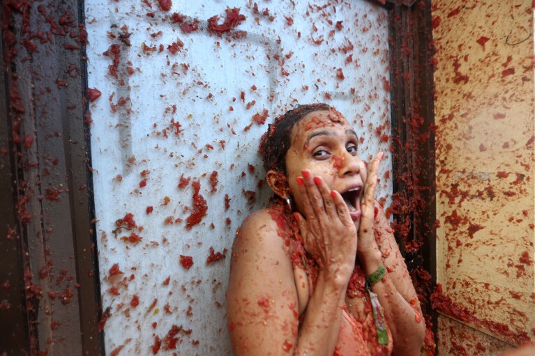 A woman reacts during the annual tomato fight fiesta called" Tomatina" in the village of Bunol near Valencia, Spain, Wednesday, Aug. 30, 2023. Thousands gather in this eastern Spanish town for the annual street tomato battle that leaves the streets and participants drenched in red pulp from 120,000 kilos of tomatoes. (AP Photo/Alberto Saiz)
