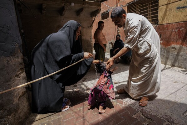 A woman sprays her children with a water hose during a heat wave outside his home in the al Fadhil neighborhood in Baghdad, Iraq, Thursday, July, 6, 2023. (AP Photo/Hadi Mizban)