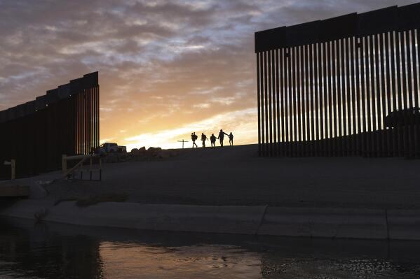 FILE - In this Thursday, June 10, 2021, file photo, a pair of migrant families from Brazil pass through a gap in the border wall to reach the United States after crossing from Mexico to Yuma, Ariz., to seek asylum. The Biden administration proposed Wednesday, Aug. 18, to change the way asylum claims are handled, aiming to cut a huge backlog of cases from the Southwest border that has resulted in people waiting years to find out if they will be allowed to stay in the U.S. (AP Photo/Eugene Garcia, File)