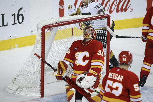 Vegas Golden Knights' Shea Theodore, top, celebrates his team's winning goal as Calgary Flames goalie Dustin Wolf reacts during overtime in an NHL hockey game in Calgary, Alberta, Saturday, April 5, 2025. (Jeff McIntosh/The Canadian Press via AP)