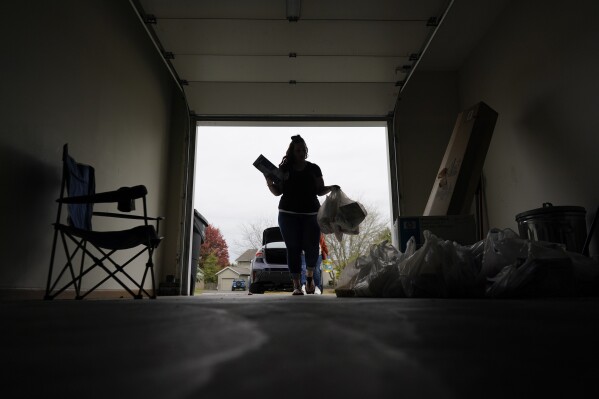 Jesse Johnson of the Family Resource Center carries groceries into client Jodi Ferdinandsen's garage after helping her shop at Walmart and driving her home in Findlay, Ohio, Thursday, Oct. 12, 2023. Earlier this year, Johnson started a job with the Family Resource Center, the same organization that employed the peer support worker who was so instrumental in her own early recovery. (AP Photo/Carolyn Kaster)