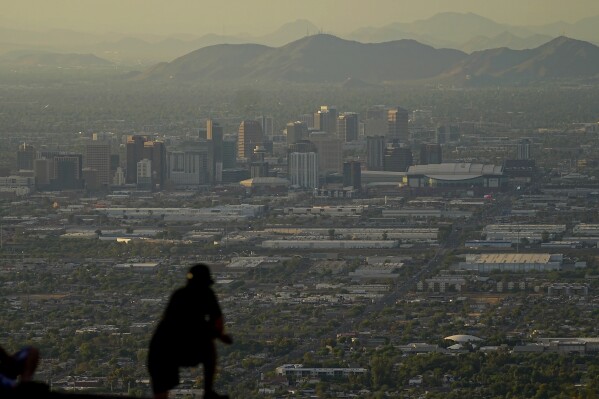A man overlooks downtown Phoenix at sunset atop South Mountain, Sunday, July 30, 2023. Phoenix hit its 31st consecutive day of at least 110 degrees Fahrenheit (43.3 Celsius). The National Weather Service says the temperature climbed to a high of 111 degrees Fahrenheit before the day was through. Some slight relief may be on the way as seasonal thunderstorms could drop temperatures in Phoenix on Monday and Tuesday. (AP Photo/Matt York)