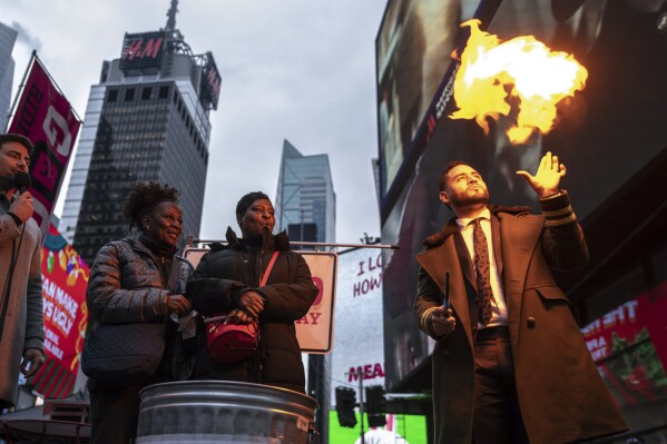 Magician Devonte Rosero, right, burns notes written by people in Times Square in New York, Thursday, Dec. 28, 2023. The burning was part an event called Good Riddance Day, where people wrote their frustrations or problems on slips of paper that were then burned, symbolizing hope for better year ahead. (AP Photo/Robert Bumsted)