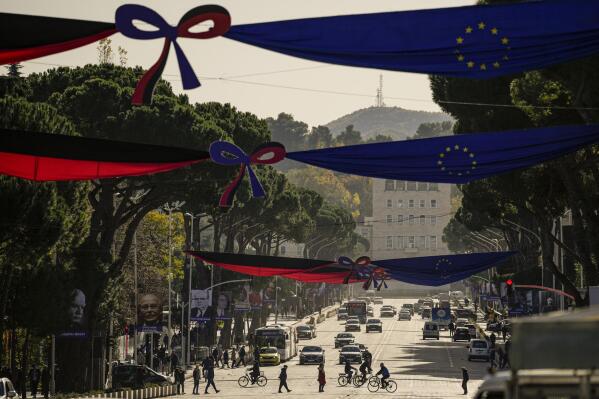 People cross the Martyrs of the Nation boulevard, decorated with Albanian and EU flags as well as portraits of personalities who had a contribution to the advancement of the European Union, in Tirana, Albania, Monday, Dec. 5, 2022. As the war in Ukraine has put the bloc's enlargement back at the top of the agenda, Albania hosts in Tirana leaders of the EU and the Western Balkans countries for a one-day summit aimed at reinvigorating the bloc's enlargement process. (AP Photo/Andreea Alexandru)