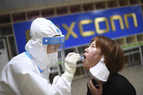 FILE - A medical worker takes a swab sample to test for COVID-19 from a worker at the Foxconn factory in Wuhan in central China's Hubei province Thursday, Aug. 5, 2021. Foxconn, the company that assembles Apple Inc.’s iPhones, has announced it is easing COVID-19 restrictions at its largest factory, in Zhengzhou, central China, that led thousands of workers to quit and drastically slowed production. (Chinatopix Via AP, File)
