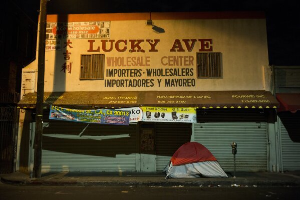
              In this Sept. 11, 2017 photo, a homeless person's tent is pitched on a sidewalk in front of the wholesale store "Lucky Ave.," in downtown Los Angeles. Up and down the West Coast, nonprofit and outreach workers with decades of experience are shocked by the surge in homeless people and in the banality of the ways they end up on the streets: a prolonged illness, a lost job, or a family crisis -- unfortunate setbacks that for many become impossible to recover from. (AP Photo/Jae C. Hong)
            