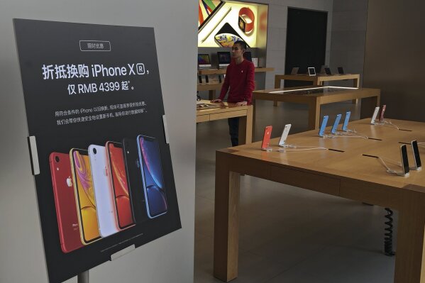 FILE - In this Jan. 3, 2019, file photo, a trade-in for iPhone XR promotion board is displayed as an Apple employee waits for customer at its retail store in Beijing, China. Apple is temporarily closing its 42 stores in mainland China, one of its largest markets, as a new virus spreads rapidly and the death toll there rose to 259 on Saturday, Feb 1, 2020. The iPhone maker said in a statement it was closing stores, corporate offices and contact centers in China until Feb. 9 “out of an abundance of caution and based on the latest advice from leading health experts." (AP Photo/Andy Wong, File)