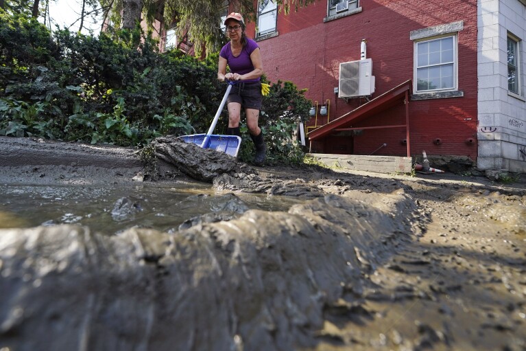 Volunteer Hazel Turrone scrapes thick mud from a downtown sidewalk, Wednesday, July 12, 2023, in Montpelier, Vt. Following a storm that dumped nearly two months of rain in two days, Vermonters are cleaning up from the deluge of water. (AP Photo/Charles Krupa)