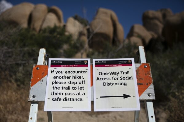 Signs advise visitors to social distance at Joshua Tree National Park in California, Tuesday, May 19, 2020. The park reopened this week after a lengthy closure to help slow the spread of the new coronavirus. (AP Photo/Jae C. Hong)