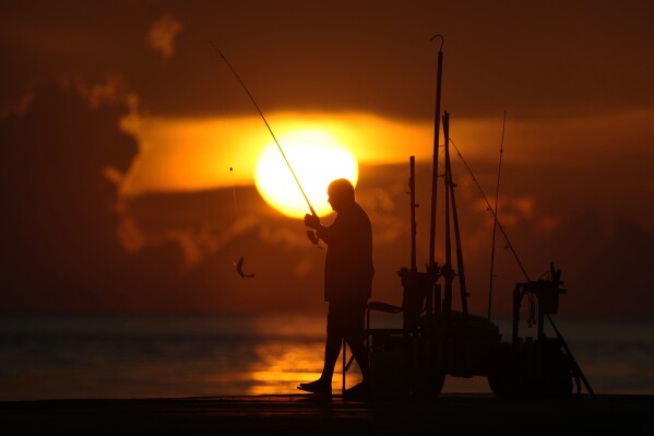 ARCHIVO - Un pescador recoge su pesca mientras el sol sale sobre el Océano Atlántico, el 28 de junio de 2023, en Bal Harbour, Florida. Una Tierra que ya se estaba calentando alcanzó su junio más caluroso registrado, con los océanos globales estableciendo récords de temperatura por tercer año consecutivo. mes, anunció el jueves 13 de julio la Administración Nacional Oceánica y Atmosférica de EE. UU. (AP Photo/Wilfredo Lee, File)