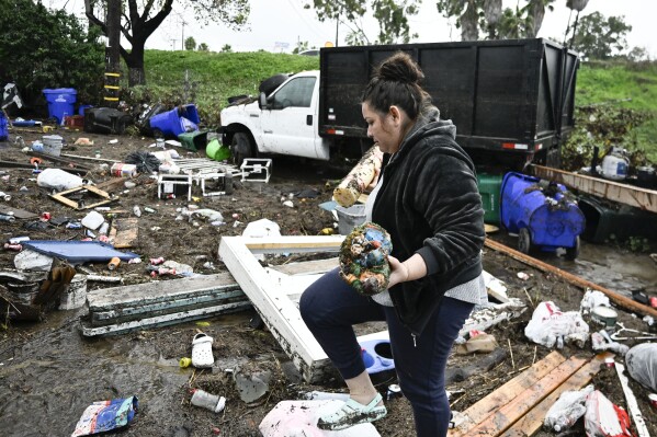 Marlene Sanchez-Barriento salavages items behind her home damaged by flooding, Tuesday, Jan. 23, 2024, in. Sanchez-(AP Photo/Denis Poroy)