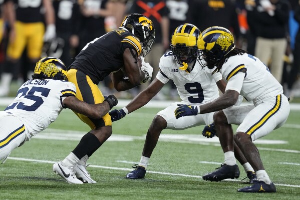 Iowa running back Leshon Williams, center, runs from Michigan linebacker Junior Colson, left, defensive back Rod Moore (9) and defensive end Jaylen Harrell, right, during the first half of the Big Ten championship NCAA college football game, Saturday, Dec. 2, 2023, in Indianapolis. (AP Photo/Darron Cummings)