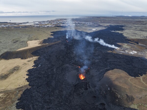 An areal view of the lava field with the main active vent, the town of Grindavik is in the background, Iceland, Monday, Jan. 15, 2024. Iceland's president says the country is battling "tremendous forces of nature" after molten lava from a volcano consumed several houses in the evacuated town of Grindavik. (AP Photo/Marco Di Marco)