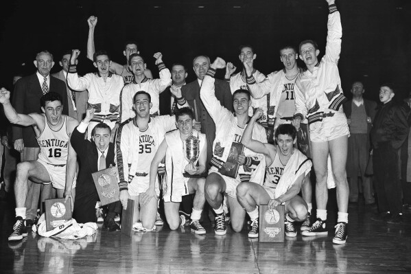 FILE - The Kentucky basketball team, which won the 1951 NCAA basketball championship, celebrates in Minneapolis, March 28, 1951, as it displays the team trophy and individual plaques. At center right is coach Adolph Rupp. Team members are, front row from left: Louis Tsioropoulos, C.M. Newton, Bobby Watson, Cliff Hagen, Lucian Whitaker and Frank Ramsey. Rear, from left: Dwight Price, Bill Spivey, Guy Strong, Roger Layne and Shelby Linville. (AP Photo/Chet Magnuson, File)