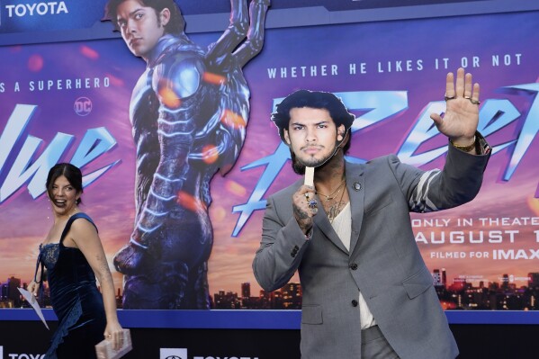 Angel Manuel Soto, right, director of "Blue Beetle," hides behind a cut-out of the film's star Xolo Mariduena as his wife, Carla Gonzalez, looks on at a screening of the film, Tuesday, Aug. 15, 2023, at the TCL Chinese Theatre in Los Angeles. Mariduena did not attend the premiere as per SAG-AFTRA guidelines during the current actors' strike. (AP Photo/Chris Pizzello)