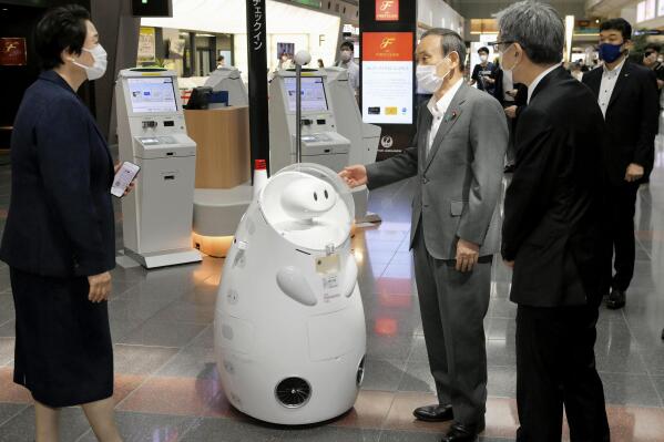 Japanese Prime Minister Yoshihide Suga, center, stands by a remotely-controlled guide robot at Haneda international airport in Tokyo, Monday, June 28, 2021. Suga inspected antigen testing for arrivals and vowed to ensure appropriate border controls as growing numbers of Olympic and Paralympic participants enter Japan ahead of the July 23 opening of the games (Kyodo News via AP)