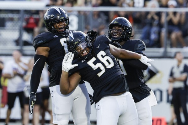 UCF Knights defensive tackle Matthew Alexander (56) celebrates with teammates defensive end Josh Celiscar, left, and defensive end Malachi Lawrence, right, after taking Villanova Wildcats quarterback during the first half of an NCAA college football game, Saturday, Sept. 16,2023, in Orlando, Fla. (AP Photo/Kevin Kolczynski)