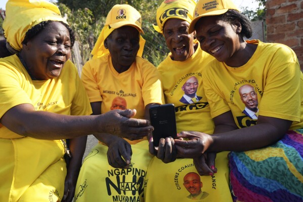 Four women huddle around a cellphone in Zimbabwe's rural Domboshava area, Wednesday, Aug. 16 2023. People in Zimbabwe's rural areas claim they are facing intimidation and a biased state-run media which limits their ability to support opposition parties ahead of national elections next week. To combat that, one group of grandmothers is using the WhatsApp messaging app to spread information from the opposition party they support in an attempt to cut through the propaganda. (AP Photo/Tsvangirayi Mukwazhi)