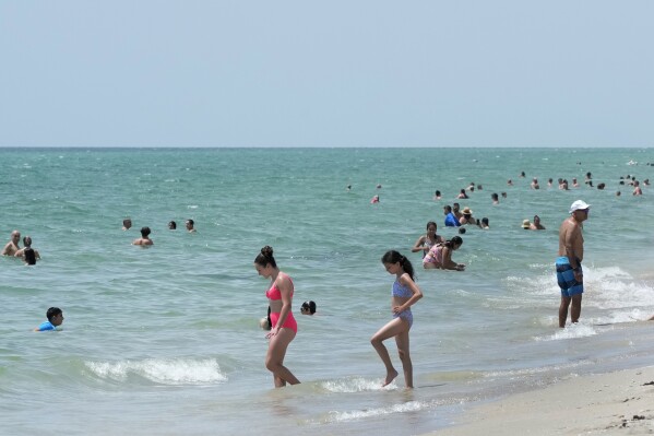 Beach goers take a dip in the Atlantic Ocean at Hollywood Beach, Monday, July 10, 2023, in Hollywood, Fla. Water temperatures in the mid-90s (mid-30s Celsius) are threatening delicate coral reefs, depriving swimmers of cooling dips and adding a bit more ick to the state's already oppressive summer weather. (AP Photo/Wilfredo Lee)